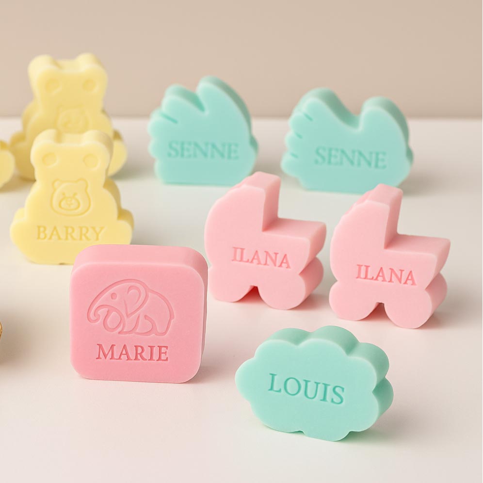 Sfeerbeeld van gepersonaliseerde zeepjes met naam als doopsuiker, in pastelkleuren en verschillende vormen zoals wolk, beer, handje en wiegje