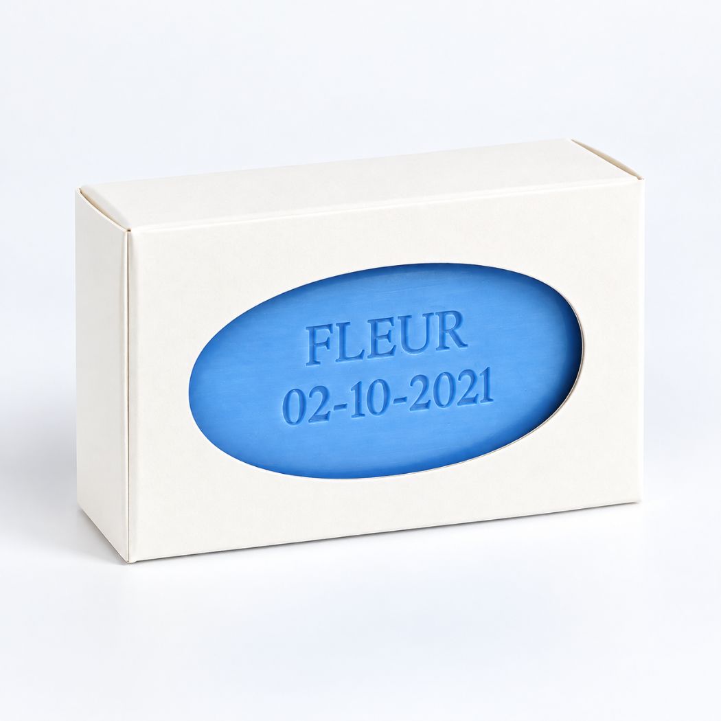 Ivoorwit kartonnen vensterdoosje met blauw zeepje met afgeronde hoeken, bedrukt met de naam Fleur en een geboortedatum.