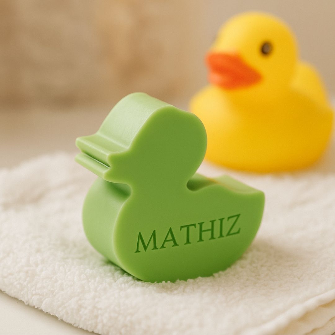 een groen zeepje in de vorm van een eendje, bedrukt met de naam MATHIZ. Op de achtergrond een geel plastiek badeendje.