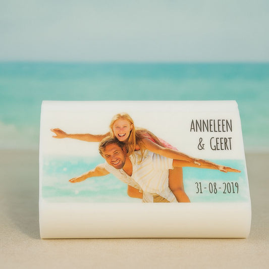Gepersonaliseerd zeepje met foto van Anneleen en Geert op het strand, namen en datum in zwart lettertype, met bijpassende zee- en luchtachtergrond.