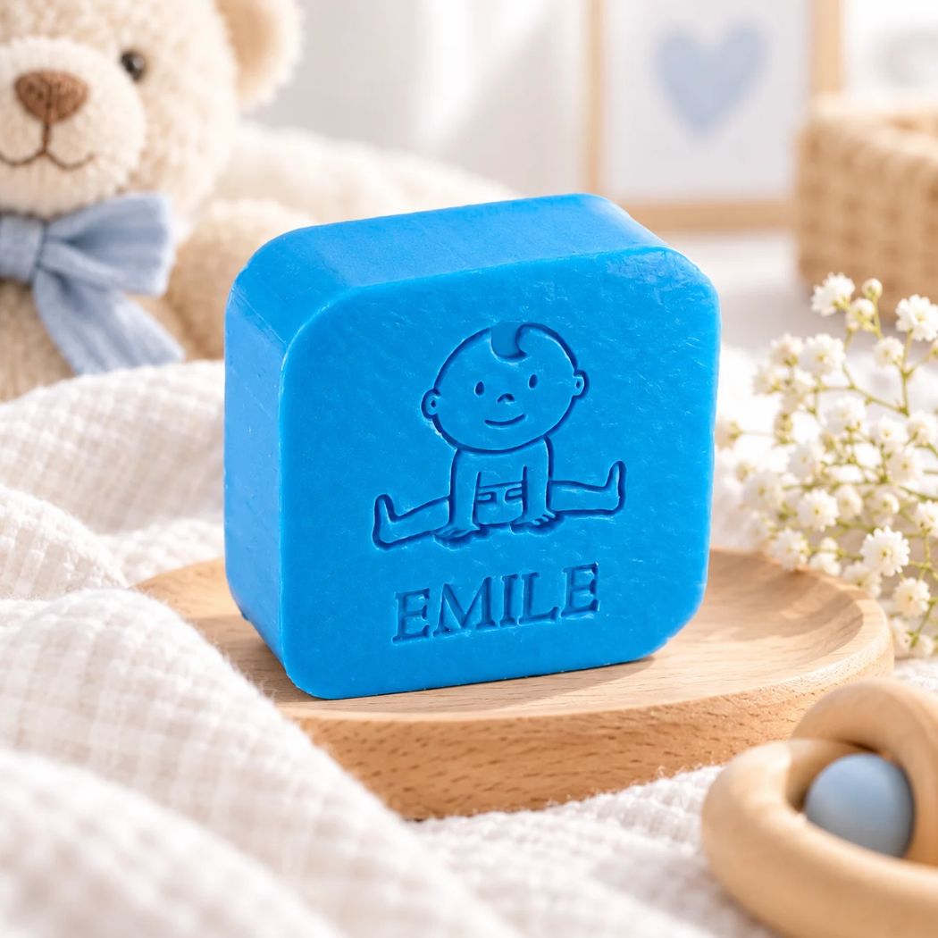 Blauw gepersonaliseerd zeepje met babyfiguur en de naam Emile, in de kleur azuur, sfeervol gepresenteerd met zachte babytextielen, houten accessoires en een teddybeer.