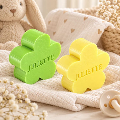 Gepersonaliseerde bloemvormige zeepjes met de naam Juliette in de kleuren appel en linde, sfeervol gepresenteerd met zachte babytextielen en houten accessoires.