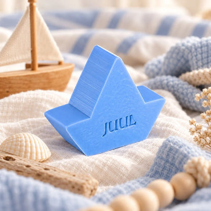 Gepersonaliseerd zeepje in de vorm van een bootje met de naam Juul in kleur Lila, sfeervol gepresenteerd in een maritieme setting met schelp, hout en zachte blauwe stoffen.