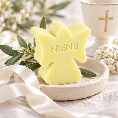 Lichtgeel zeepje in de vorm van een engel met de naam Niene, sfeervol gepresenteerd als communiebedankje met witte accenten, groen blad en een gouden kruis op de achtergrond.