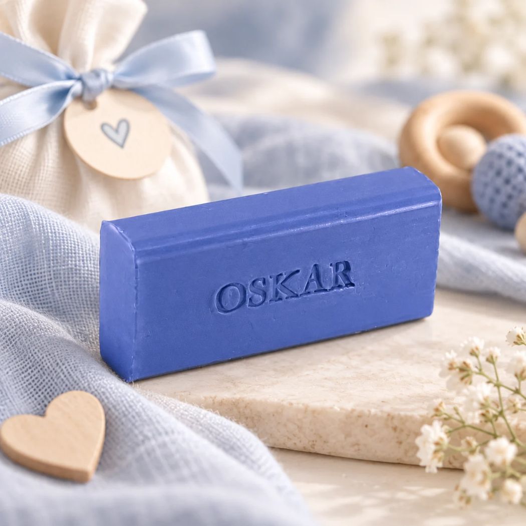 Gepersonaliseerd rechthoekig zeepje met de naam Oskar in de kleur mure, sfeervol gepresenteerd met blauwe babytextielen en houten accessoires.