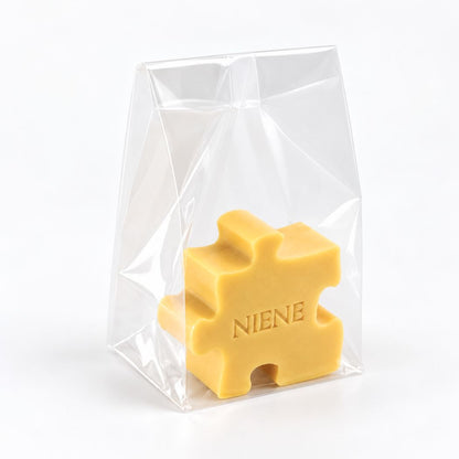 Gepersonaliseerd zeepje in de vorm van een puzzelstuk met de naam Niene, in de kleur kamperfoelie, verpakt in een transparant zakje op een lichte achtergrond.
