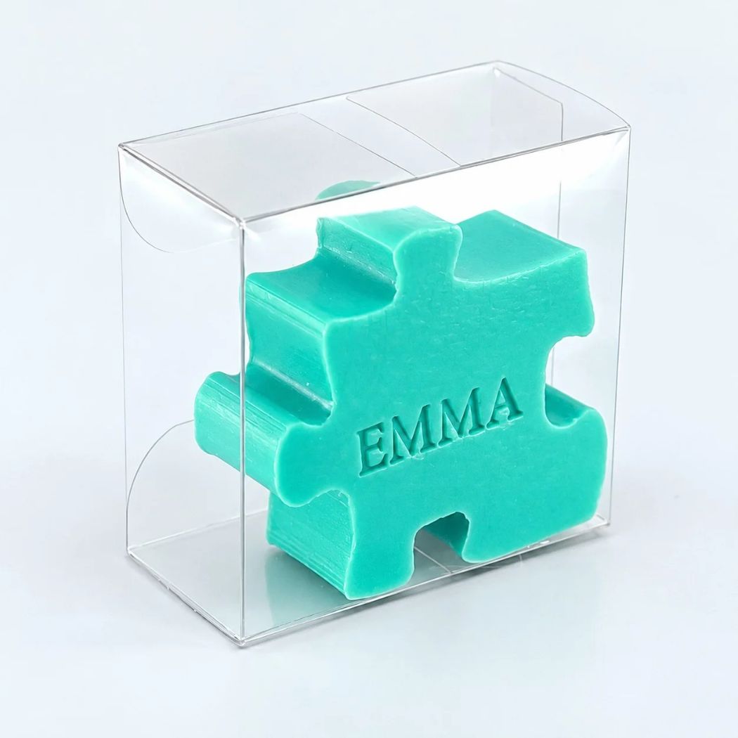 Gepersonaliseerd zeepje in de vorm van een puzzelstuk met de naam Emma, in de kleur zeealgen, verpakt in een transparant doosje op een lichte achtergrond.