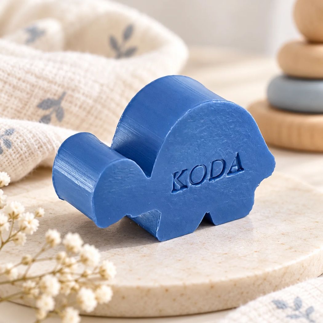 Gepersonaliseerd schildpadzeepje met de naam Koda in de kleur mure, sfeervol gepresenteerd met lichte textiel, houten accessoires en zachte blauwe accenten.