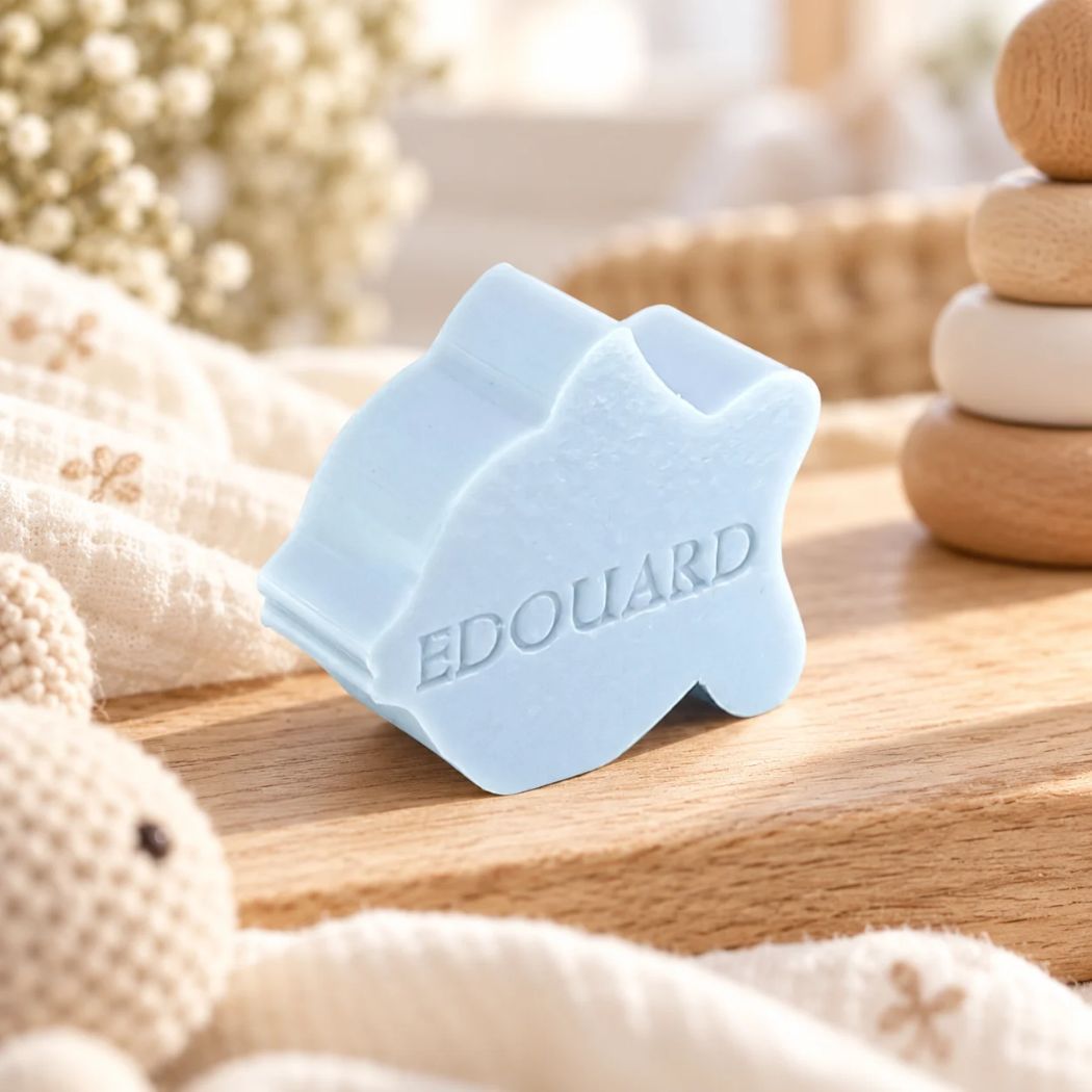 Lichtblauw zeepje in de vorm van een vis met de naam Edouard, sfeervol gepresenteerd op een houten ondergrond met zachte stoffen en neutrale babyaccessoires.