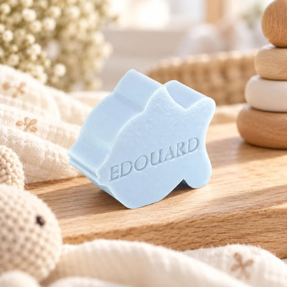 Lichtblauw zeepje in de vorm van een vis met de naam Edouard, sfeervol gepresenteerd op een houten ondergrond met zachte stoffen en neutrale babyaccessoires.