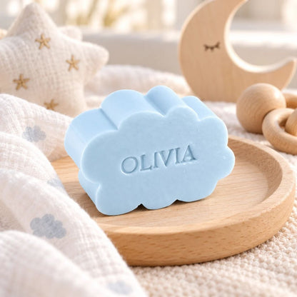 Lichtblauw zeepje in de vorm van een wolkje met de naam Olivia, sfeervol gepresenteerd op een houten schaaltje met zachte stoffen en houten maan- en sterdecoratie.