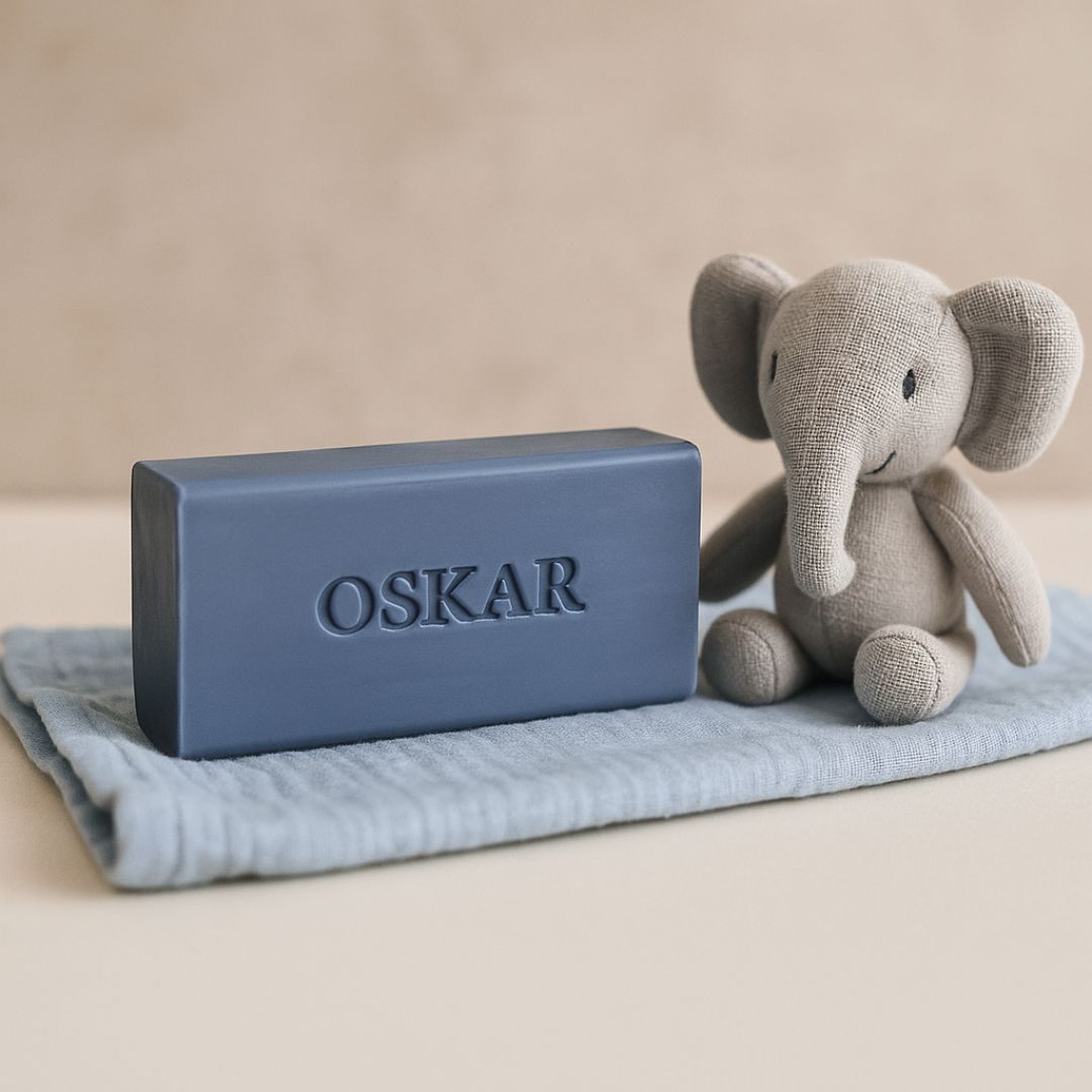 Donkerblauw mini baar zeepje met naam OSKAR op een zachtblauw tetra doekje. Rechts staa een grijs olifantje.