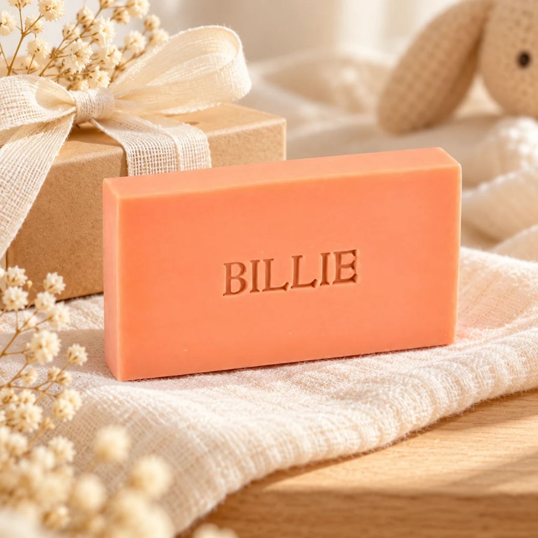Gepersonaliseerd koraalkleurig zeepje met de naam Billie, sfeervol gepresenteerd met een cadeaudoosje, lint en zachte babyaccessoires.